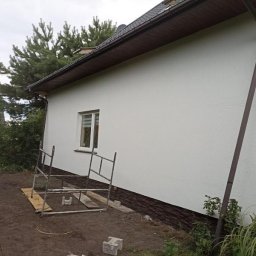 Usługi remontowo-budowlane Łukasz Lamparski - Elewacja domu po renowacji, widoczne rusztowanie i fragment brązowego orynnowania, świeżo pomalowana ściana w jasnym odcieniu.