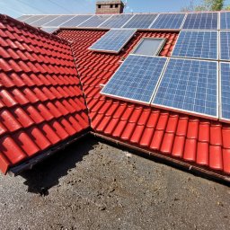 Usługi remontowo-budowlane Łukasz Lamparski - Czerwony dach z dachówki ceramicznej z zamontowanymi panelami fotowoltaicznymi i oknem dachowym, widok z dołu.
