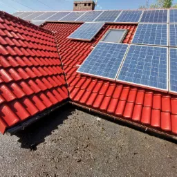 Czerwony dach z dachówki ceramicznej z zamontowanymi panelami fotowoltaicznymi i oknem dachowym, widok z dołu.