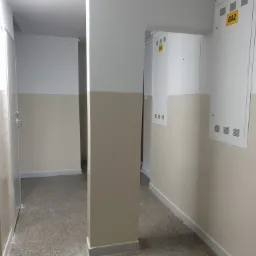 Korytarz w budynku z pomalowanymi ścianami na biało i beżowo, widoczne szafki gazowe.