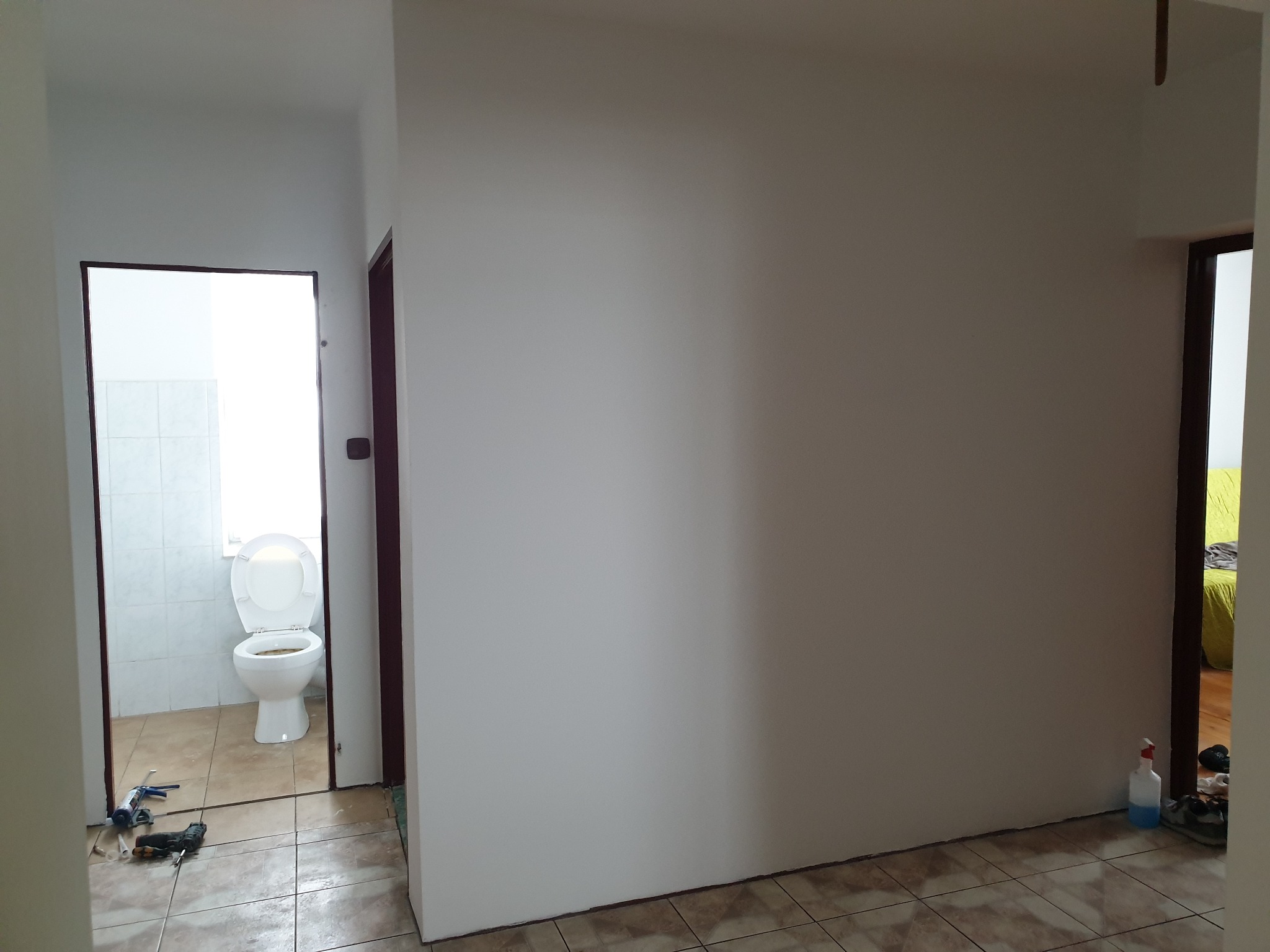 Świeżo pomalowany pokój z widokiem na toaletę z otwartą klapą i narzędziami malarskimi na podłodze.