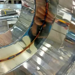 Błyszczący, spawany element z nierdzewnej stali w kształcie pierścienia, widoczne ślady spawania z charakterystycznymi przebarwieniami termicznymi, odbicie dłoni w polerowanej powierzchni.