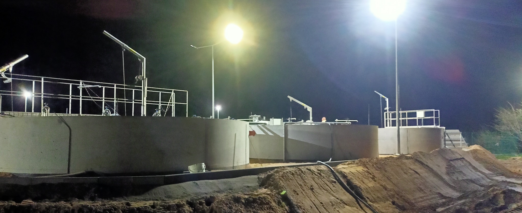 Budowa zbiorników przemysłowych nocą, widoczne oświetlenie placu budowy i elementy konstrukcji stalowych.
