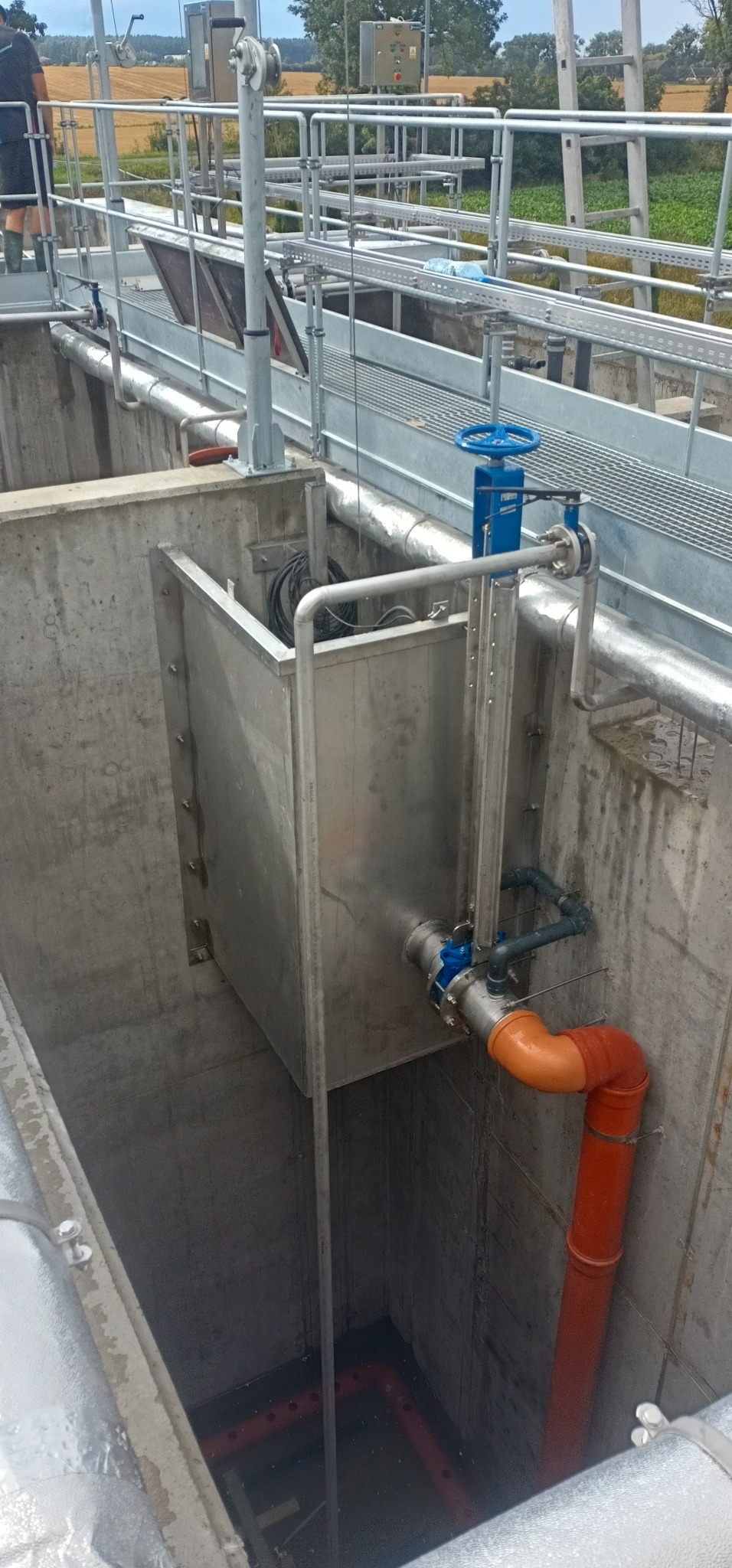 Widok z góry na betonowy zbiornik z metalową konstrukcją, rurami i zaworami w instalacji przemysłowej.