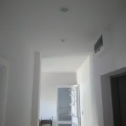 Wnętrze korytarza z pomalowanymi na biało ścianami, widoczne oświetlenie sufitowe, klimatyzator na ścianie, metalowa szafa i krzesło w tle.