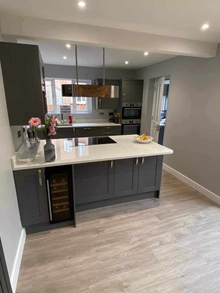 Nowoczesna kuchnia w odcieniach szarości z wyspą, na której znajduje się płyta indukcyjna i wazon z kwiatami, a pod nią wbudowana chłodziarka do wina.