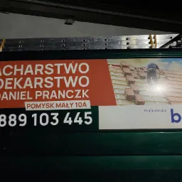 Reklama firmy dekarskiej i blacharskiej Daniel Pranczk umieszczona na samochodzie dostawczym, prezentująca układanie dachówki na dachu. Widoczne logo BAT.