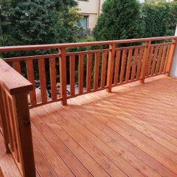 Woodcraft - Drewniany taras z balustradą w odcieniach brązu, widok z boku, zieleń w tle.