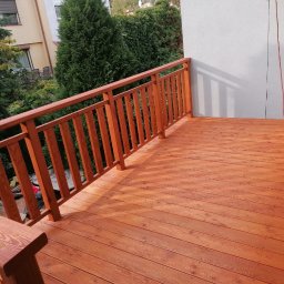 Woodcraft - Drewniany taras z balustradą w odcieniach brązu, świeżo po impregnacji, widok z góry, w tle zieleń drzew i fragment budynku.