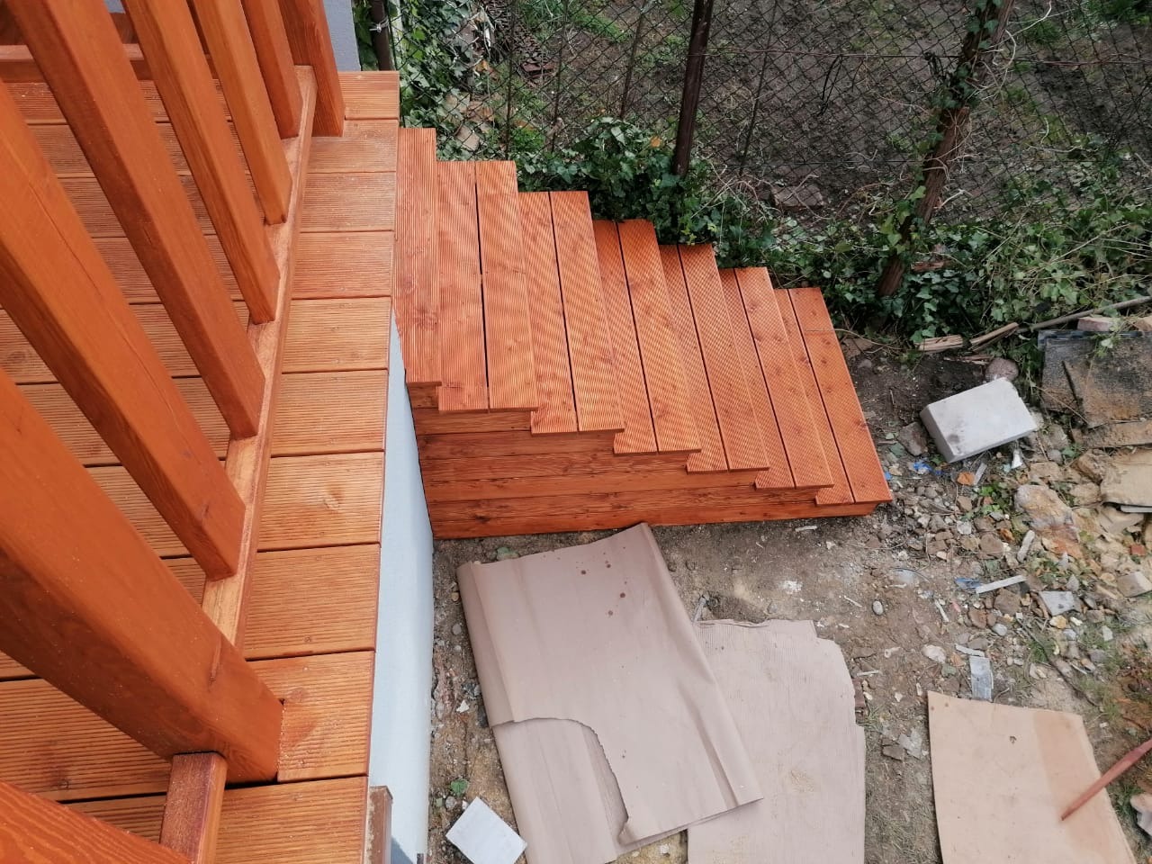 Drewniane schody zewnętrzne w trakcie budowy, widok z góry, surowe otoczenie budowy z ziemią i materiałami budowlanymi.