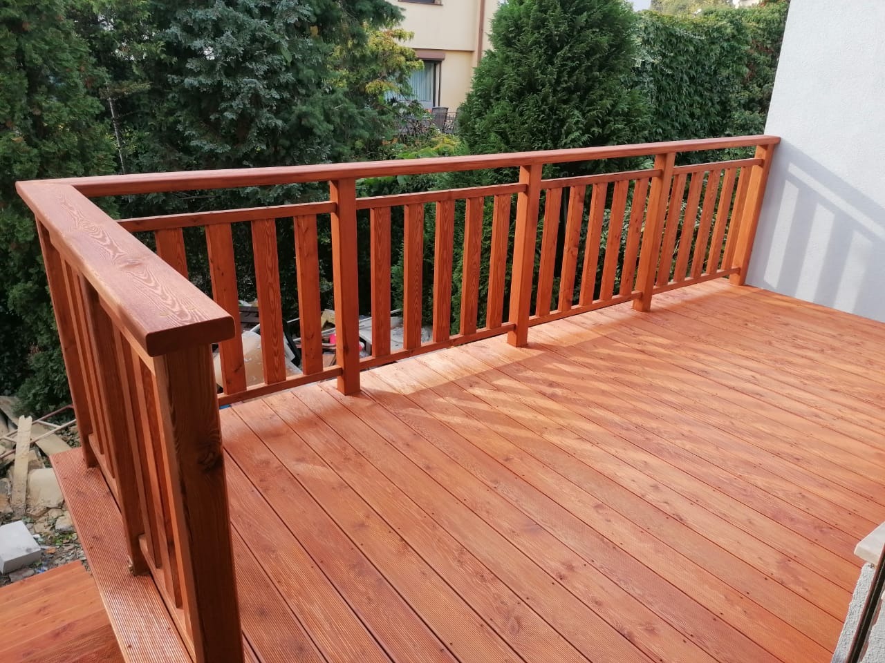 Drewniany taras z balustradą w odcieniach brązu, widok z boku, zieleń w tle.