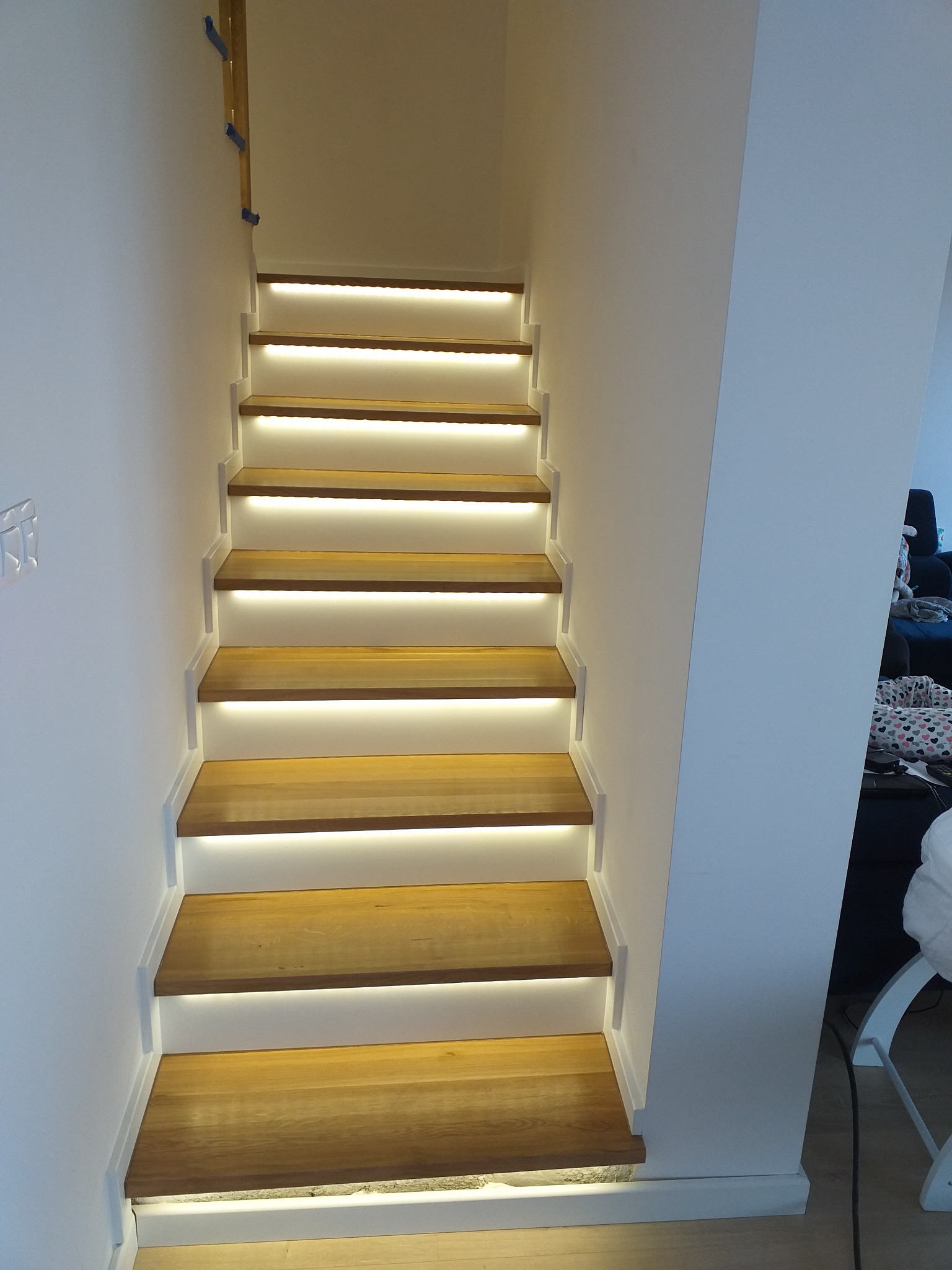 Nowoczesne schody z drewna z podświetleniem LED zamontowanym pod każdym stopniem, widok z dołu w górę.