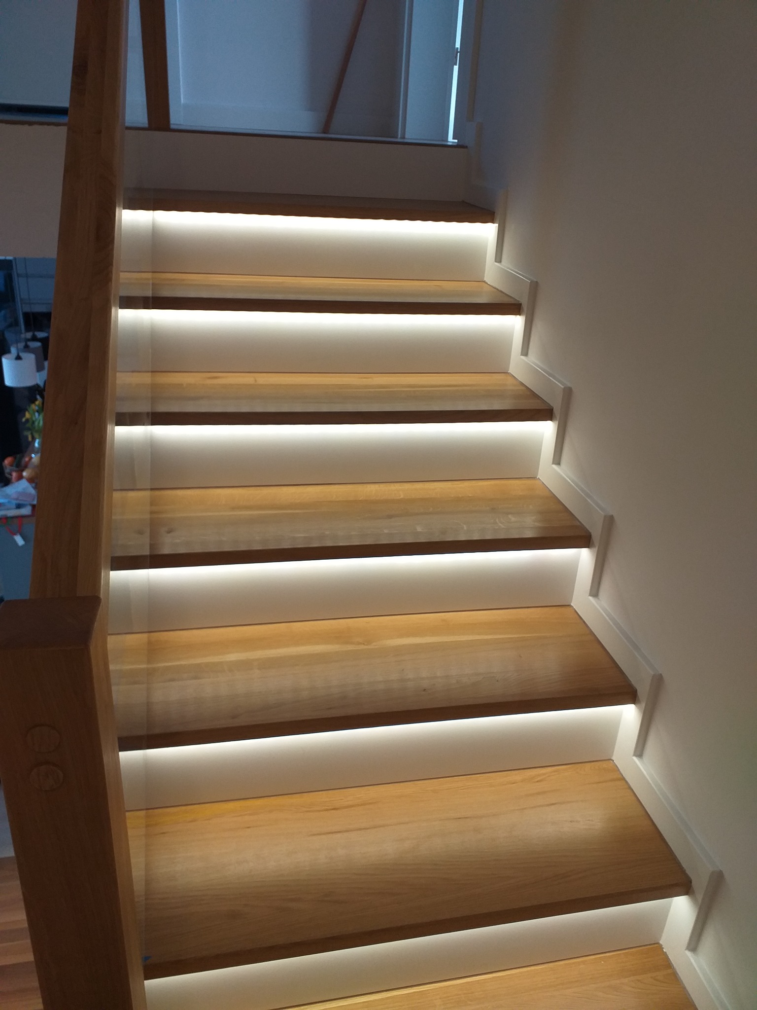 Drewniane schody z podświetleniem LED, widok z dołu, jasne drewno, białe boki, nowoczesny design.