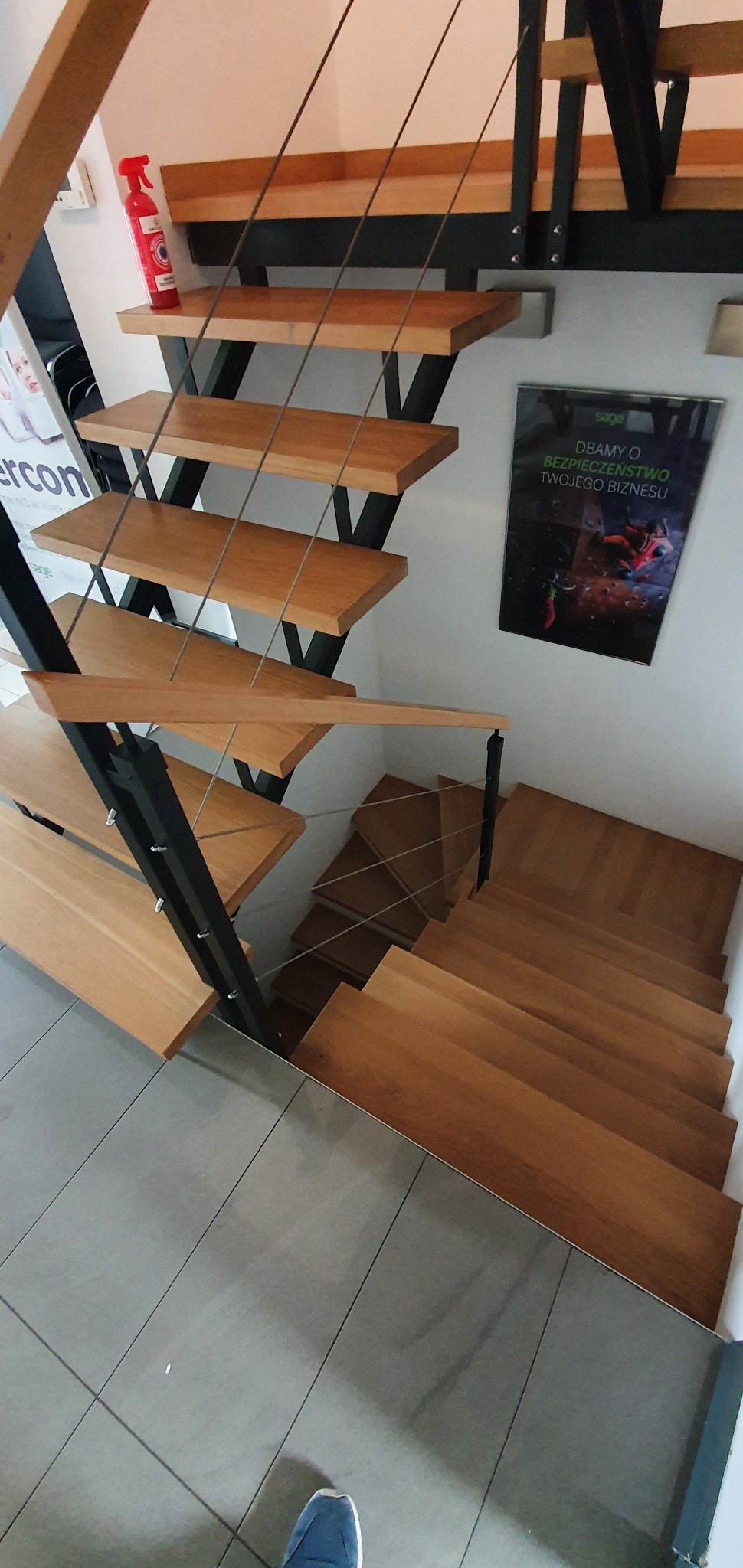 Nowoczesne schody z drewnianymi stopniami i metalową konstrukcją, widok z góry, z akcentem na minimalistyczny design i zabezpieczenia linkami stalowymi.