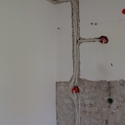 Ivan Demidov - Białe przewody elektryczne ułożone w bruzdach w ścianie, widoczne puszki instalacyjne w kolorze pomarańczowym, ściana częściowo otynkowana, widoczna cegła.