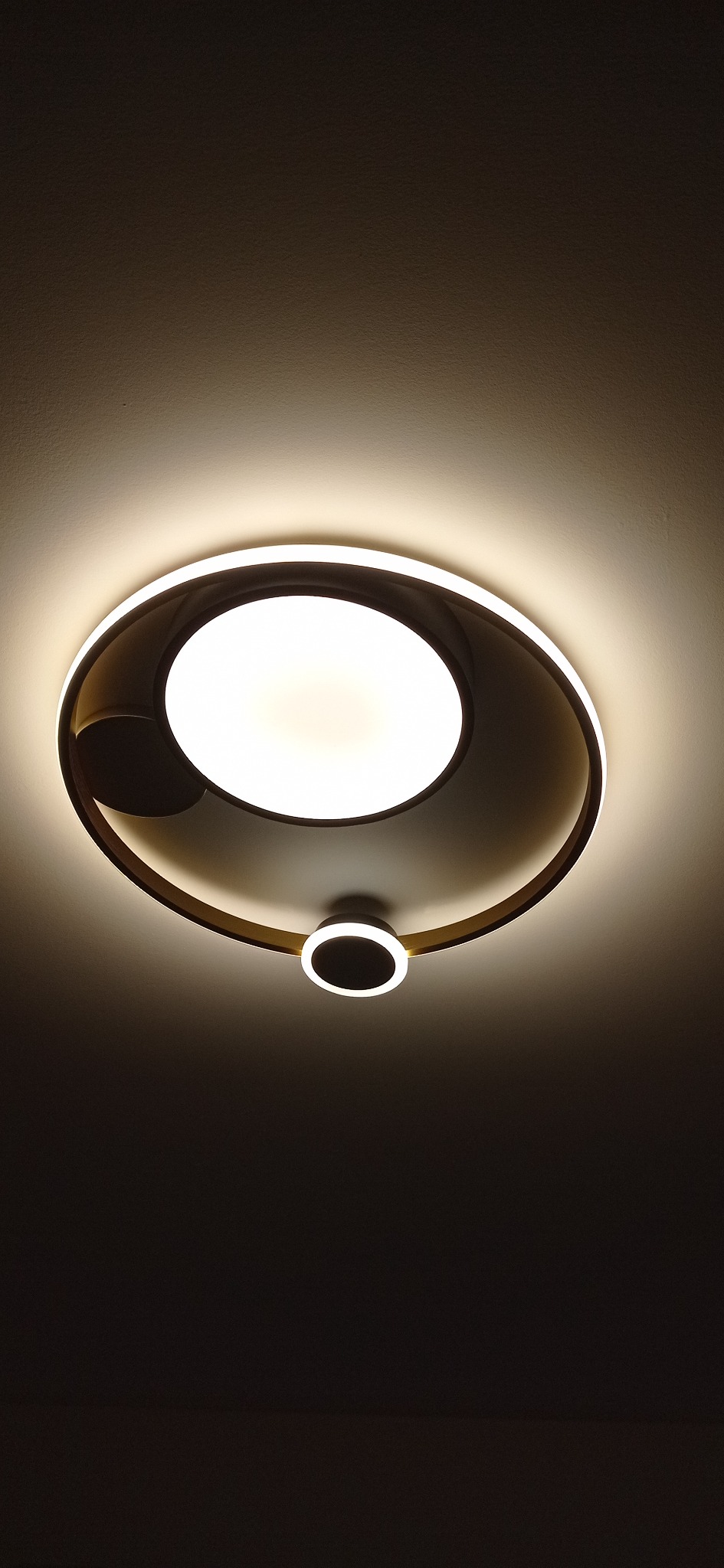 Nowoczesna lampa sufitowa LED z okrągłym kloszem i dodatkowym, mniejszym elementem oświetleniowym, zamontowana na białym suficie.