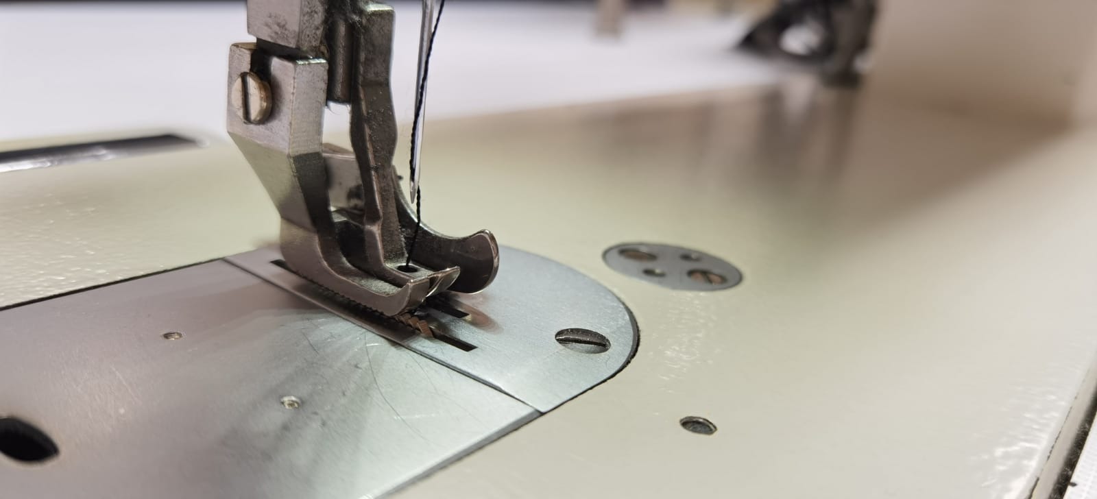 Stopka maszyny do szycia z igłą i czarną nicią, zbliżenie na metalową płytkę z rowkiem.