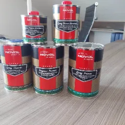 Pięć puszek z preparatami marki Novol dla klasycznych samochodów: Epoxy Thinner, Polycoat Protect i Epoxy Primer, ustawione na drewnianym biurku w biurze.