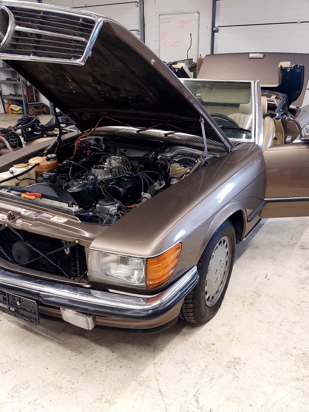 Brązowy kabriolet Mercedes z otwartą maską silnika podczas naprawy w warsztacie w Zgłobniu, widoczne narzędzia i części zamienne.