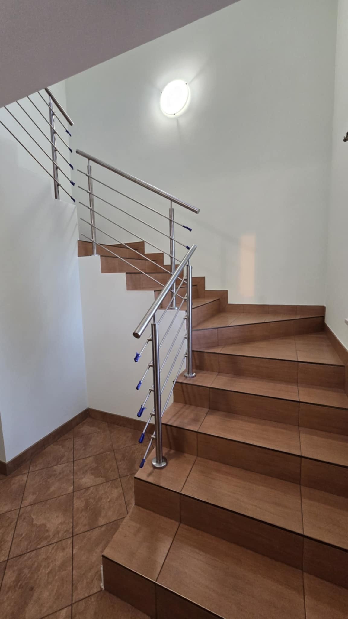 Schody wyłożone brązowymi płytkami z balustradą ze stali nierdzewnej z niebieskimi zaślepkami, widok z dołu.