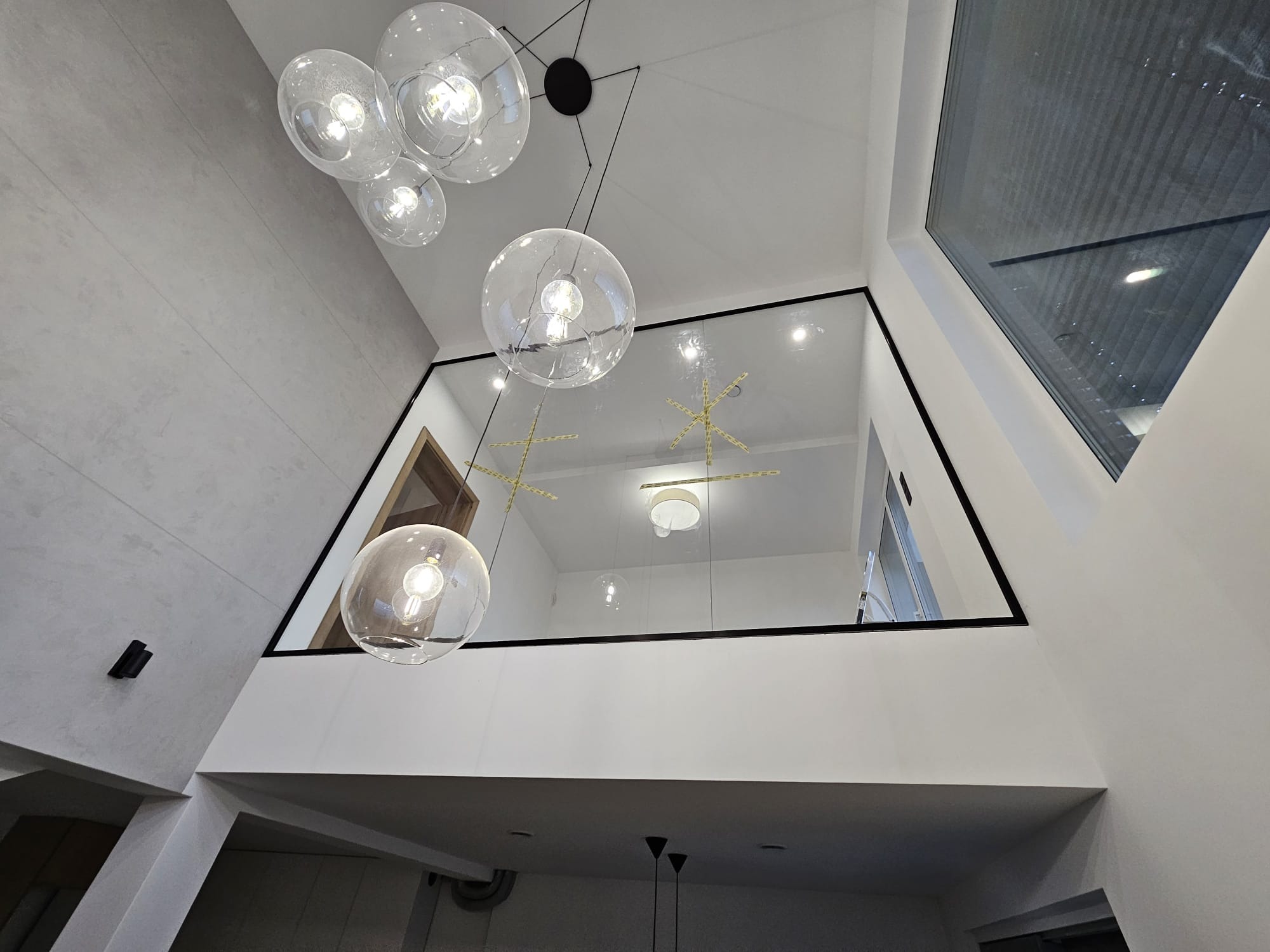 Szklana balustrada na antresoli z czarną ramą, widok z dołu na kuliste lampy wiszące i okno dachowe.