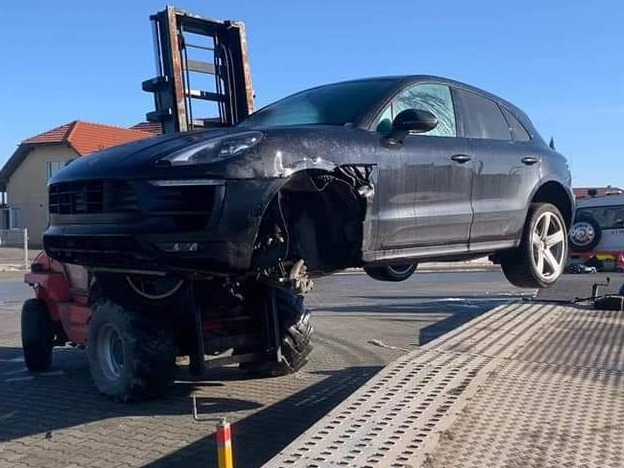 Czarny samochód osobowy marki Porsche bez przedniego koła, podniesiony na wózku widłowym na zewnątrz.