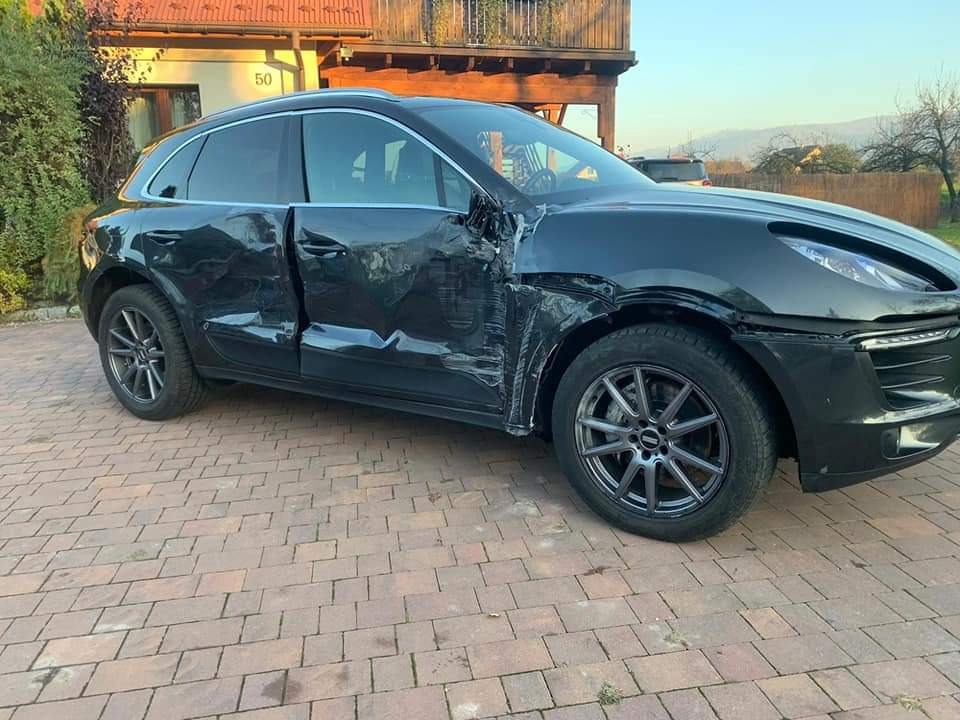 Uszkodzony czarny samochód osobowy marki Porsche Macan po kolizji drogowej, widoczne wgniecenia i zarysowania karoserii, brak przedniego zderzaka, uszkodzone drzwi kierowcy.