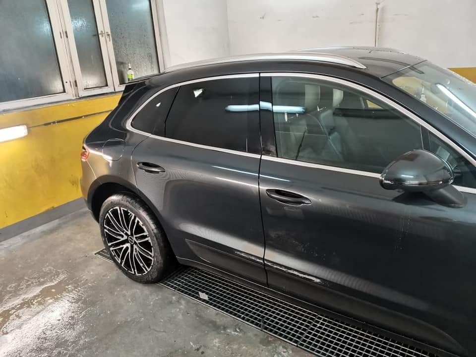 Szary samochód Porsche Macan po umyciu w myjni, widoczne krople wody na karoserii, czarne felgi z srebrnymi elementami, metalowa krata w posadzce.