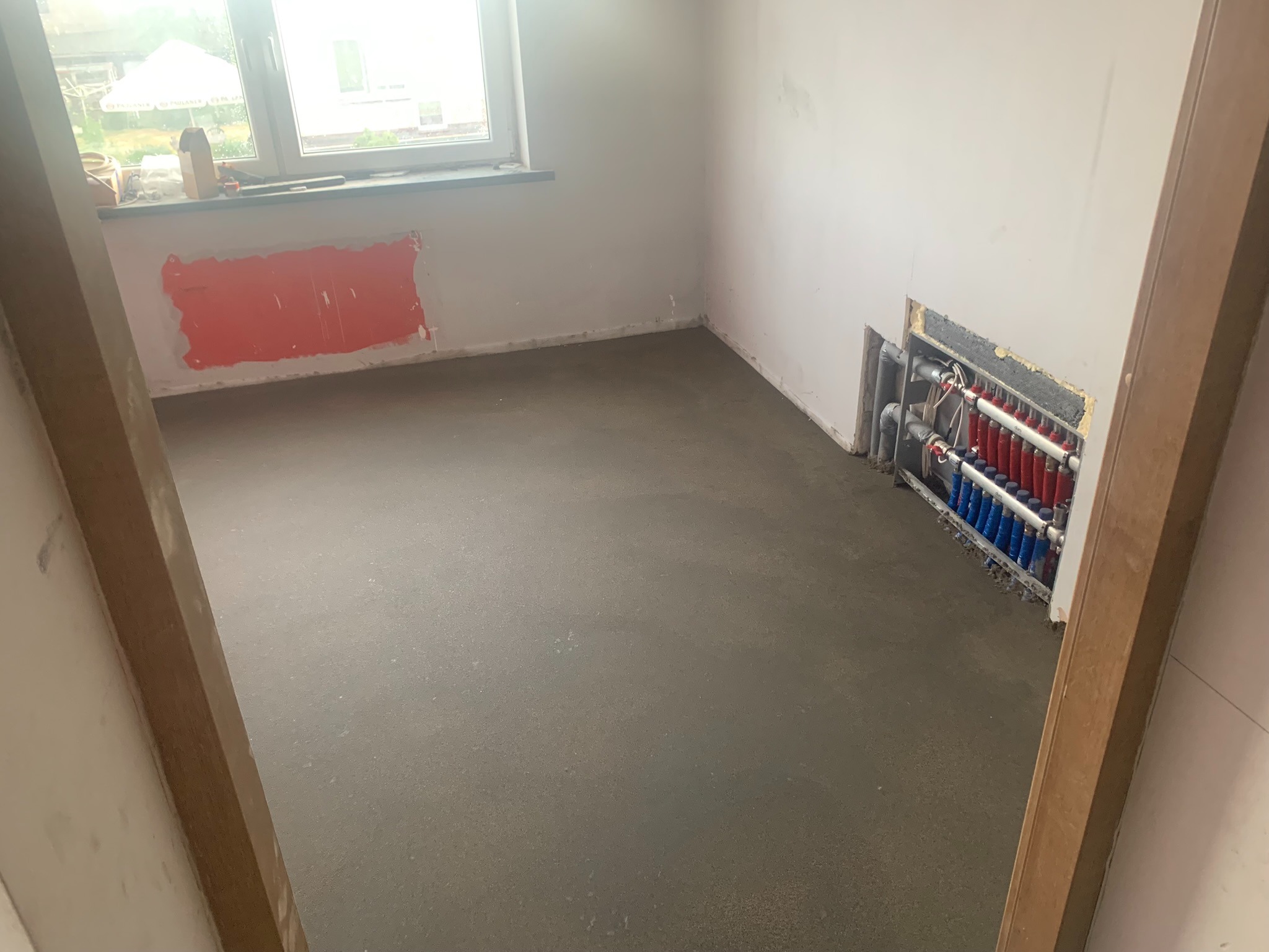 Wylewka podłogowa w trakcie schnięcia w pomieszczeniu w Bysławiu, z widocznym systemem ogrzewania podłogowego w ścianie.