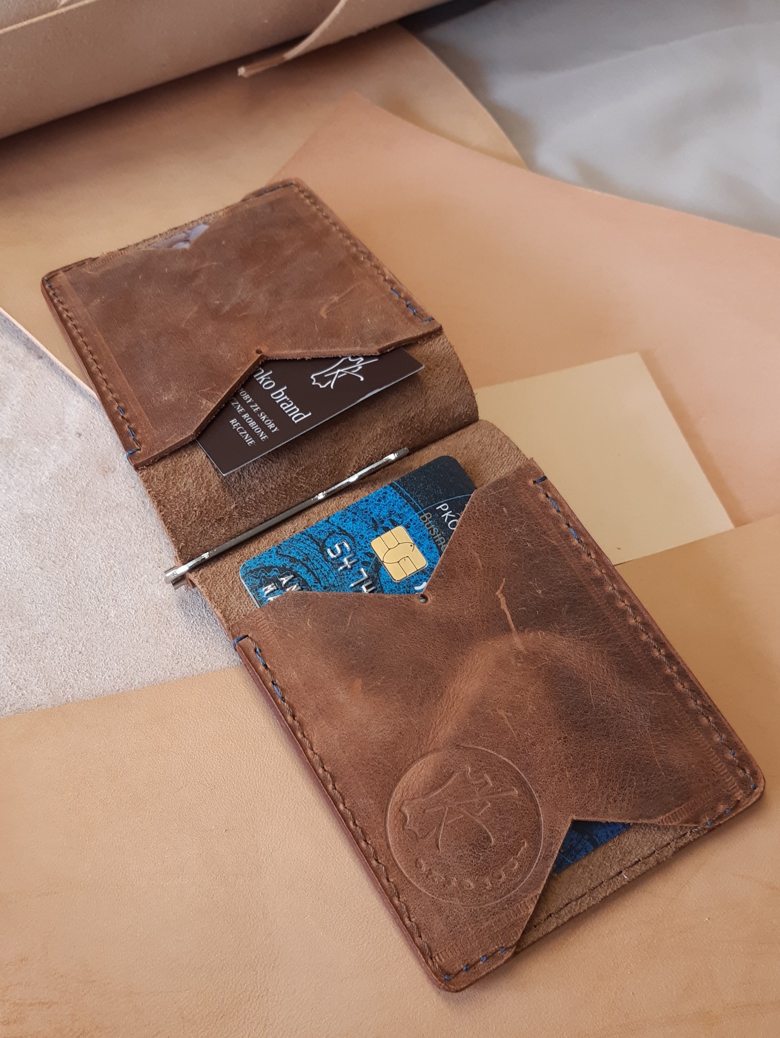 Otwarty, brązowy, skórzany portfel na karty z widoczną kartą płatniczą i wizytówką, leżący na skórzanym tle.