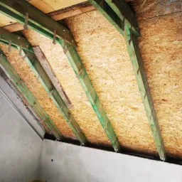 Konstrukcja dachu poddasza z zielonymi belkami i płytą OSB, widok od wewnątrz budynku w trakcie prac wykończeniowych.