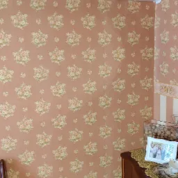 Biały klimatyzator Hyundai zamontowany na ścianie z różową tapetą w kwiaty, widoczny fragment drewnianej komody i stolika nocnego z budzikiem.