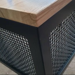 Wytwórnia i Wyroby z Drutu Łukasz Kraska - Metalowa konstrukcja z drewnianym blatem, czarne profile i ażurowa siatka. Detal mebla w stylu industrialnym, widok z bliska na róg konstrukcji.