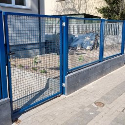 Wytwórnia i Wyroby z Drutu Łukasz Kraska - Niebieska, metalowa siatka ogrodzeniowa z bramką, osadzona na betonowej podmurówce. Widok z zewnątrz posesji na fragment chodnika i domu w tle.