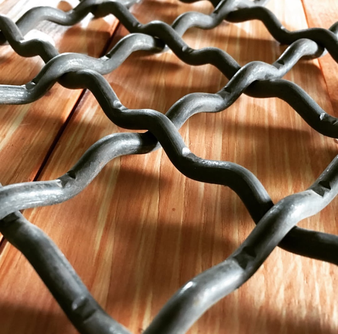 Metalowa krata z dekoracyjnymi zgrubieniami na tle drewnianych desek, ukazana z niskiej perspektywy.