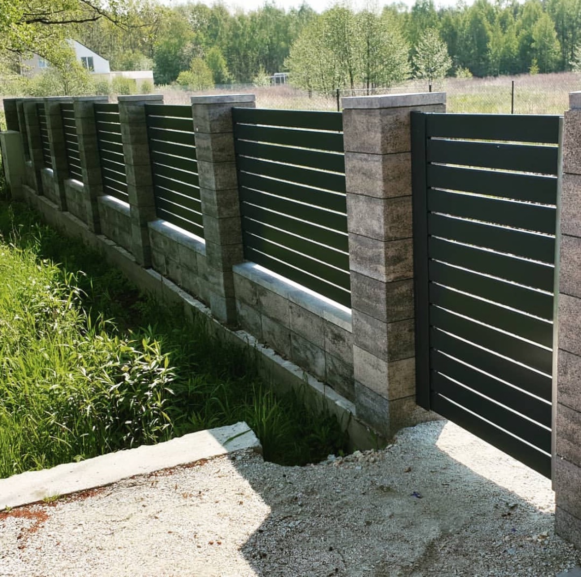 Nowoczesne ogrodzenie panelowe z bramą w kolorze grafitowym, z poziomymi szczeblami, wsparte na słupkach z szarej kostki. Otoczenie: trawa i drzewa.
