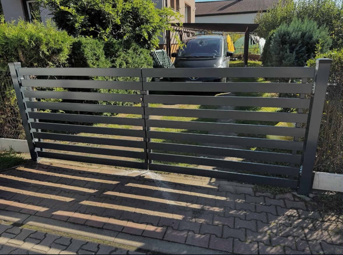 Nowoczesna, pozioma brama wjazdowa w kolorze grafitowym, z widocznym samochodem w tle i kostką brukową na podjeździe, w słoneczny dzień.