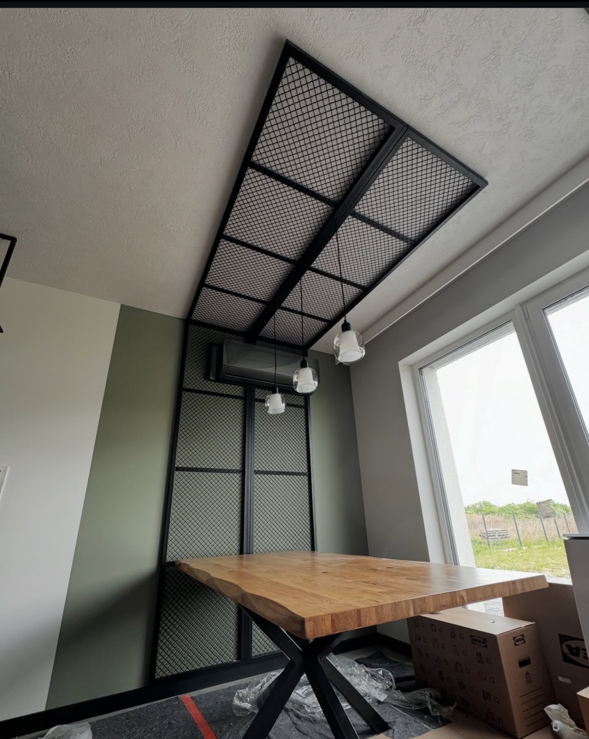 Nowoczesna, metalowa konstrukcja z siatki, zamontowana na suficie i ścianie, tworząca unikalny element dekoracyjny wnętrza z drewnianym stołem.