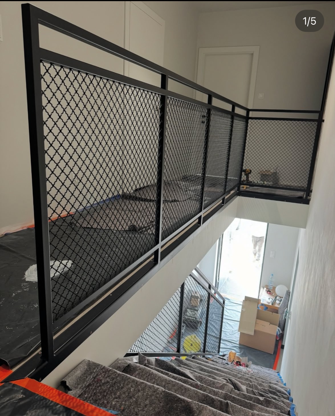 Nowoczesna, czarna balustrada schodowa z metalową siatką o dekoracyjnym wzorze, zamontowana w jasnym wnętrzu. Widok z góry na dół schodów.