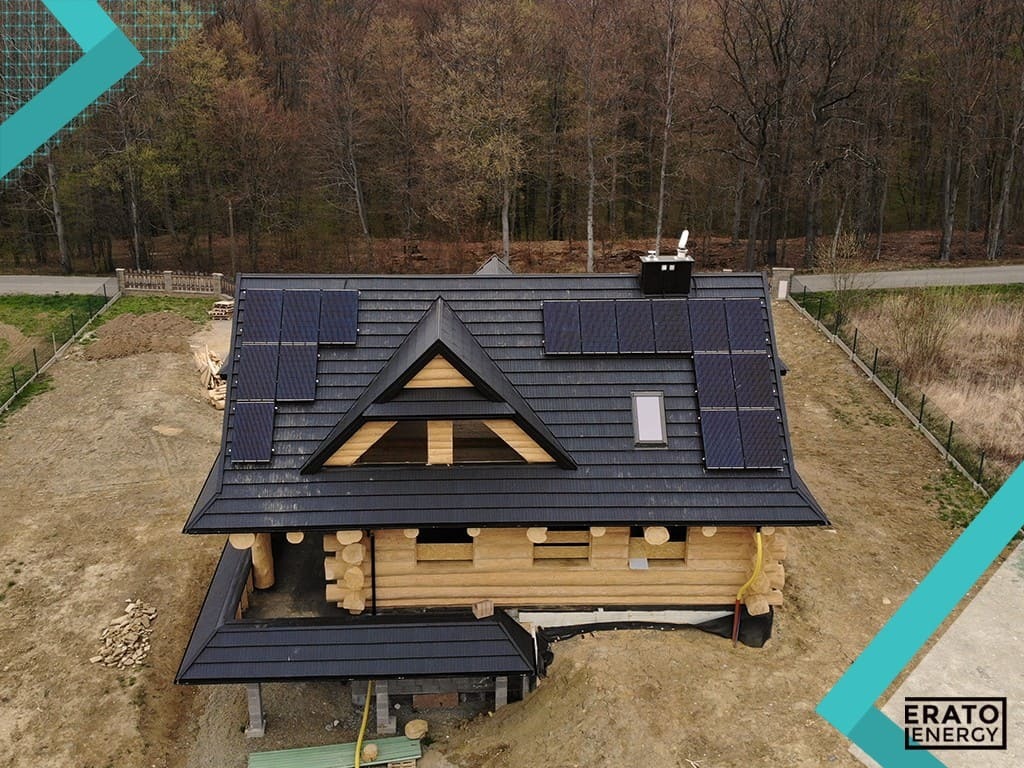 Drewniany dom w stylu góralskim z czarnym dachem pokrytym panelami słonecznymi, widok z góry w słoneczny dzień, w tle las.