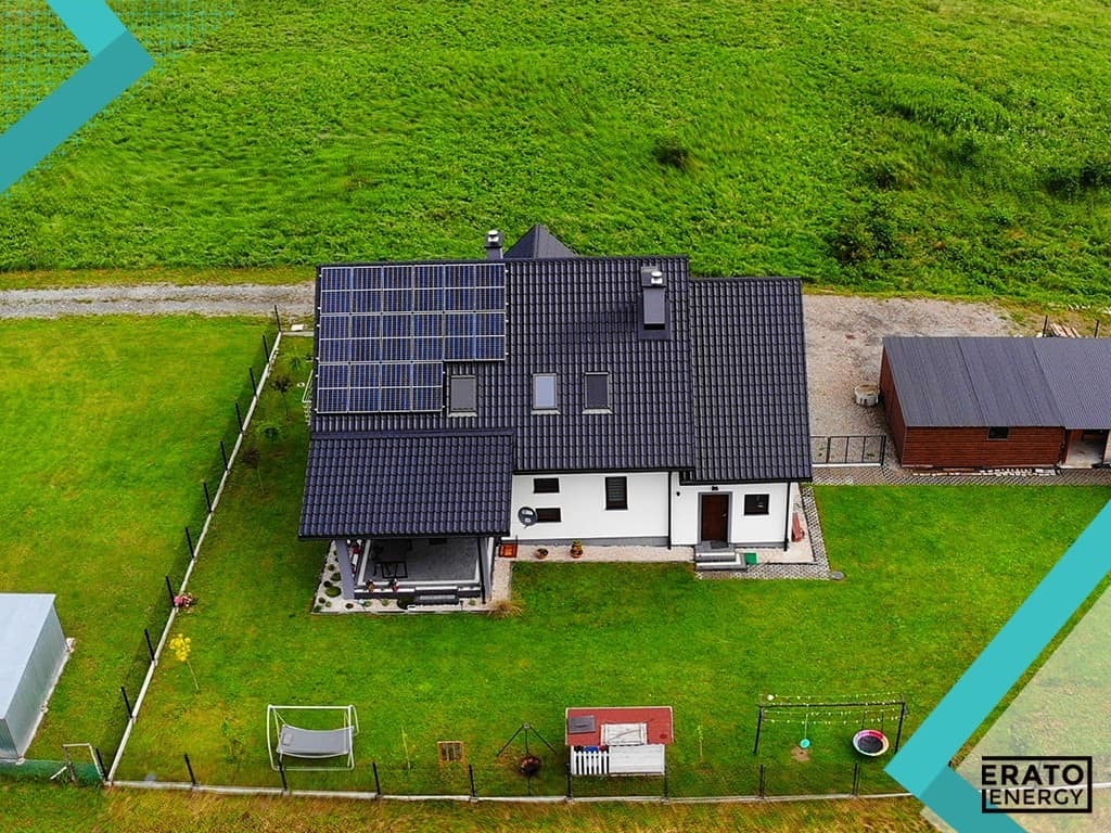 Dom jednorodzinny z panelami fotowoltaicznymi na dachu, widok z lotu ptaka, zielone otoczenie, logo firmy w rogu.