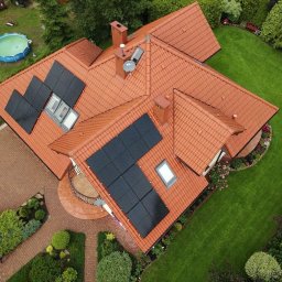 Wojciech Pawluczuk - Widok z góry na dom z czerwoną dachówką i panelami słonecznymi, zadbany ogród, basen w tle.