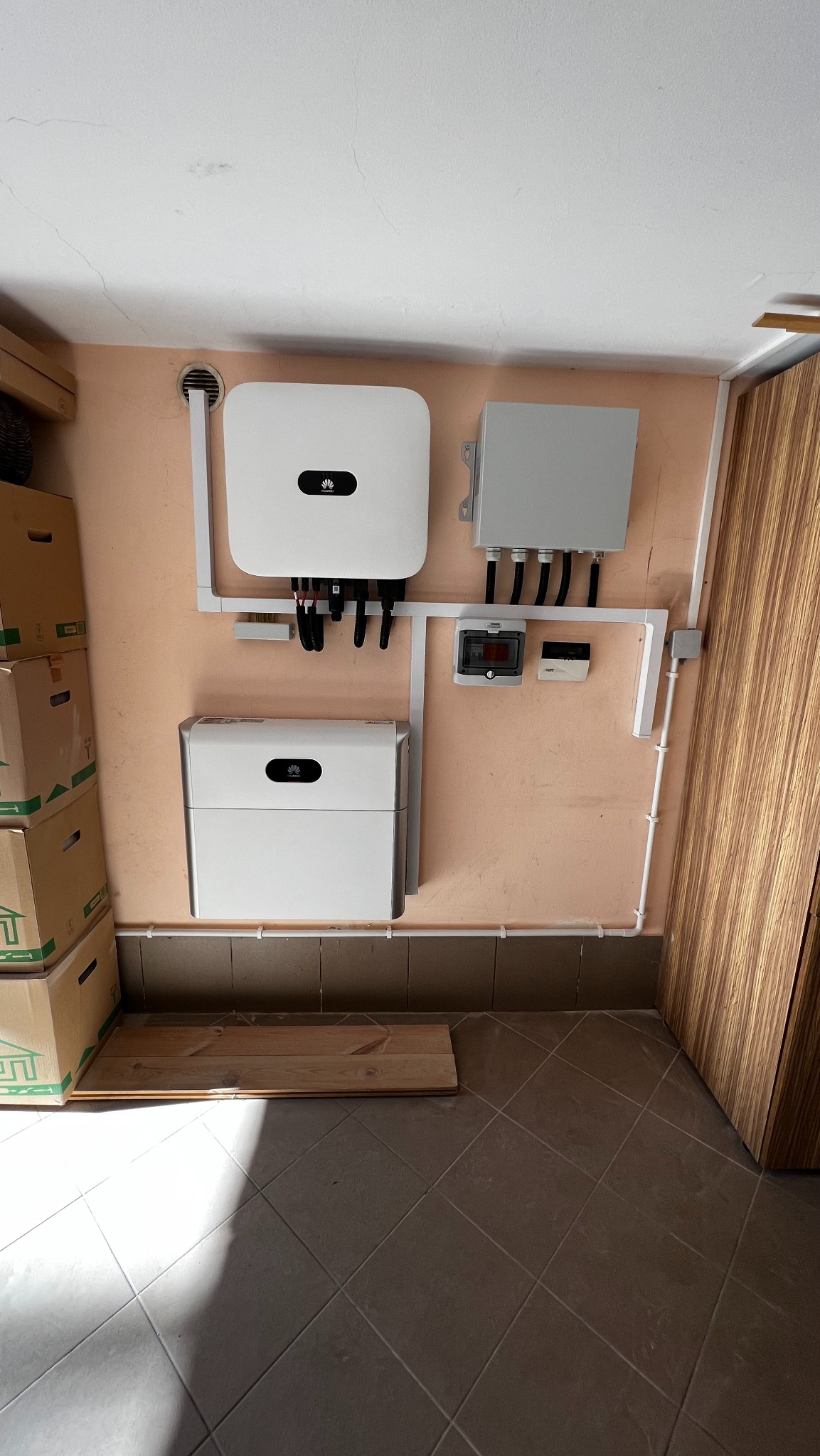 Zamontowany inwerter i magazyn energii firmy Huawei na pomarańczowej ścianie, widoczne kable i zabezpieczenia, na podłodze leżą deski.