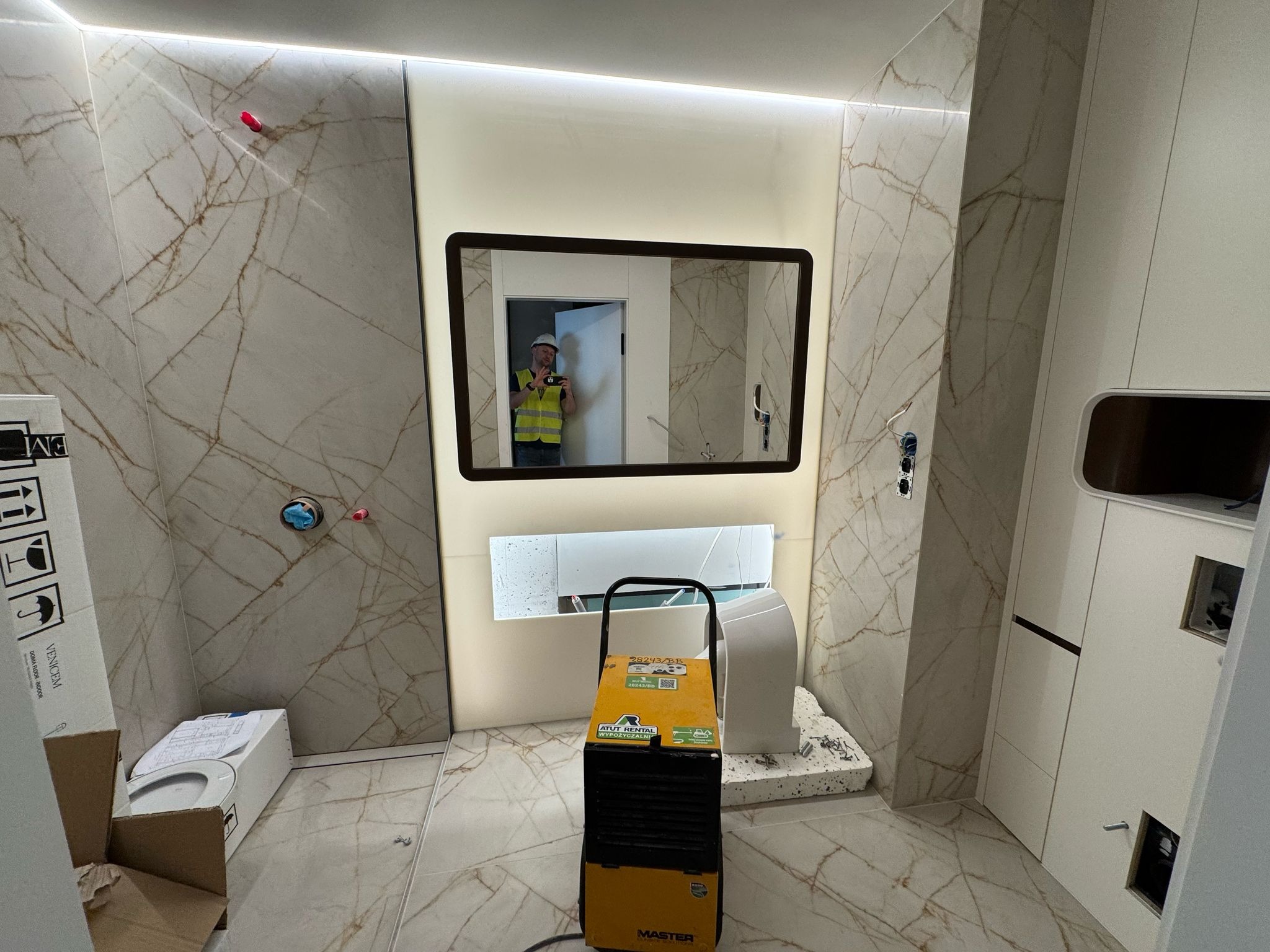 Wykończona łazienka w Słubicach z marmurowymi płytkami i podświetlanym lustrem. Widoczny osuszacz powietrza i elementy armatury w trakcie montażu.