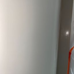 Spray-Tech - Świeżo pomalowana, jasna ściana w rogu pomieszczenia, zabezpieczona folią malarską, widoczne delikatne refleksy światła.