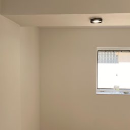 Spray-Tech - Świeżo pomalowane wnętrze z widocznym oknem, na parapecie butelki z wodą i narzędzia, sufit z zamontowanym oświetleniem punktowym.