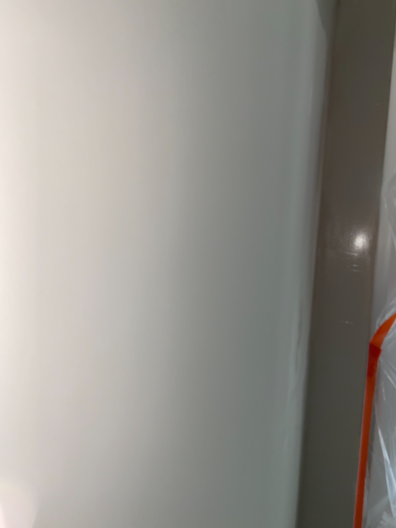 Świeżo pomalowana, jasna ściana w rogu pomieszczenia, zabezpieczona folią malarską, widoczne delikatne refleksy światła.