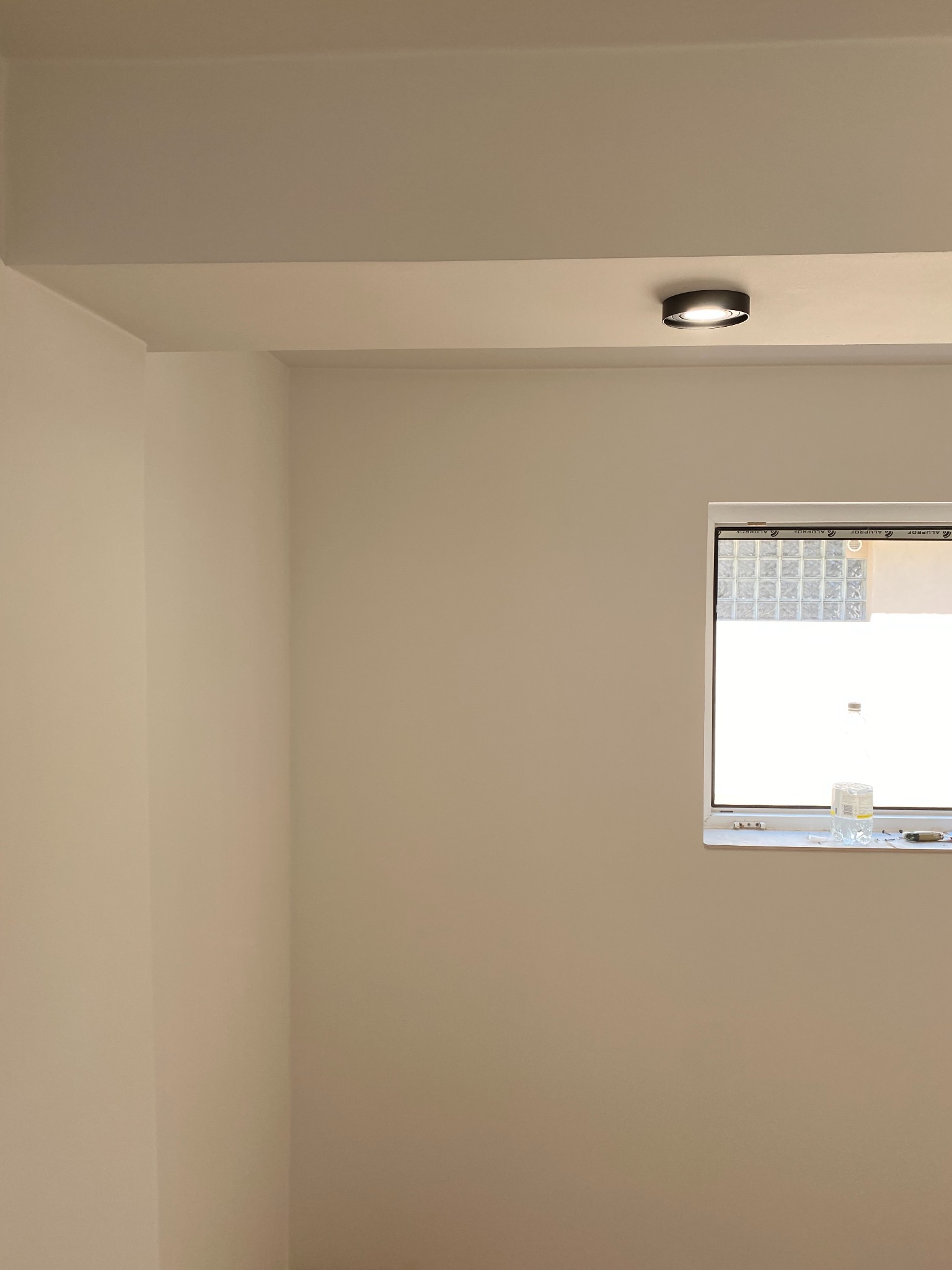 Świeżo pomalowane wnętrze z widocznym oknem, na parapecie butelki z wodą i narzędzia, sufit z zamontowanym oświetleniem punktowym.