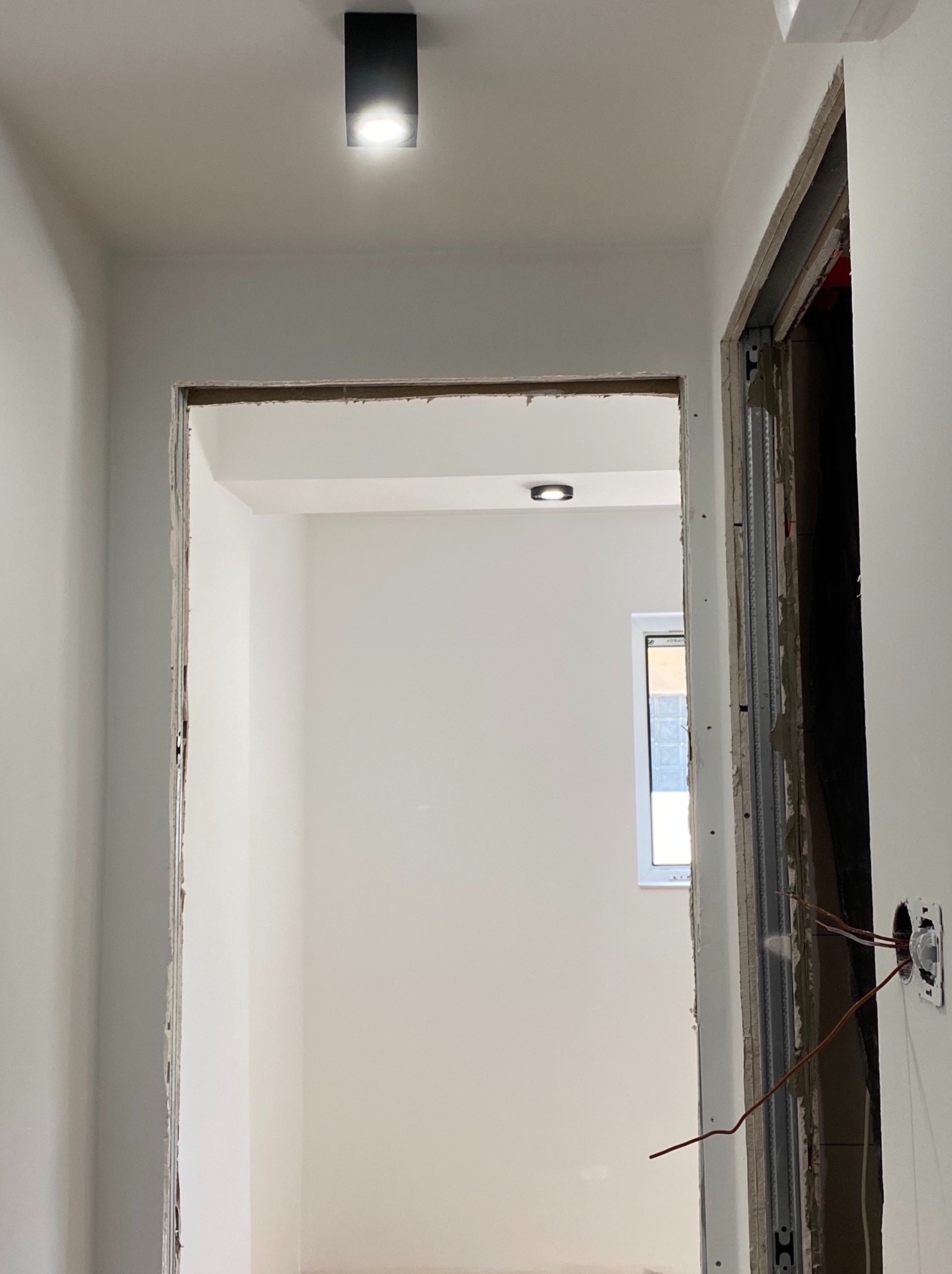 Wnętrze w trakcie remontu: widok na przygotowane do wykończenia przejście między pomieszczeniami, z widocznymi przewodami elektrycznymi i surowymi krawędziami ścian.