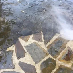 Czyszczenie ciśnieniowe kamiennej ścieżki, widoczne różnice w kolorze między czystą a brudną powierzchnią, strumień wody z dyszy.